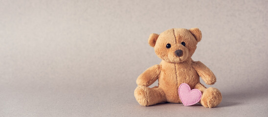 Small teddy bear with a pink heart on a beige background. Side view, selective focus, copy space. Valentine's Day. Banner