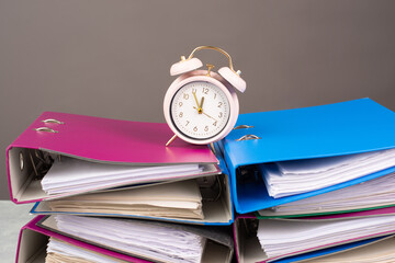 Alarm clock standing on pile of file folders, burnout, stress and overworked, pressure at work,...