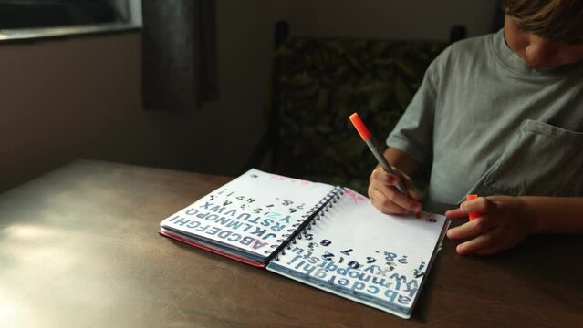 Young student diligently prints letters in his notebook, trying to make each line smooth and neat. 