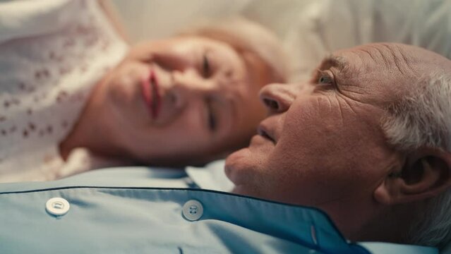 Close-up of happy elderly couple lying in bed and talking, close relationship