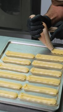 A pastry chef makes eclairs in a bakery. eclairs are baked in the oven. eclair production process. pastry bag with dough	