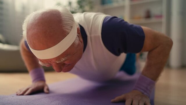 Senior man in funny sportswear trying to do push-ups at home, falling on floor
