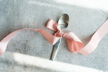Elegant spoon with pink ribbon on textured background