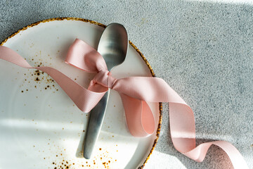 Elegant spoon with pink ribbon on a textured plate