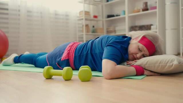 Funny senior woman in sportswear napping on fitness mat instead of exercising