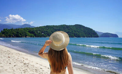 Holidays in Brazil. Back view of bikini girl walking on Ubatuba tropical beach, Brazil.