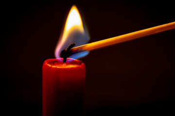 A red candle is lit by a match