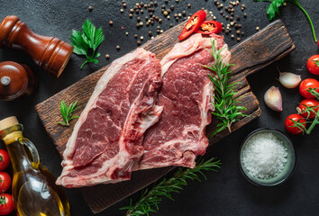 Two raw beef steak on wooden board on dark stone background top view