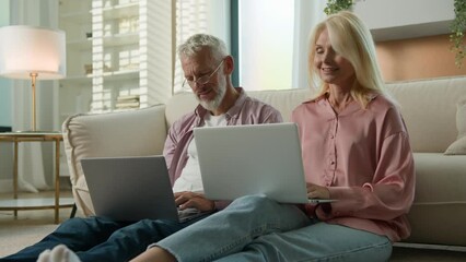 Caucasian smiling family couple man woman grandparents working remote on floor in living room at home using computer application check email closing laptops high five celebrating success job well done
