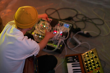 High angle view with selective focus on unrecognizable male sound producer dressed in white T-shirt and yellow beanie hat working with musical equipment