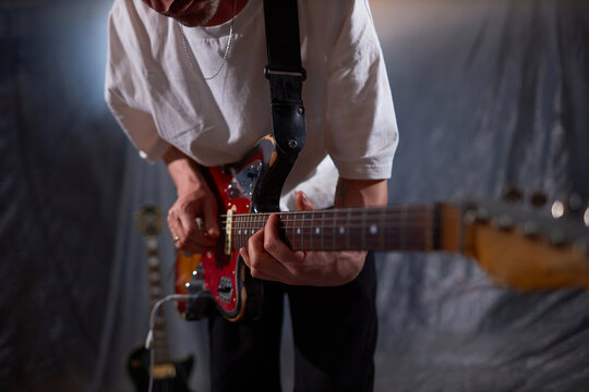 Cropped shot of male musician playing electric guitar on black strap at rehearsal base preparing for live show