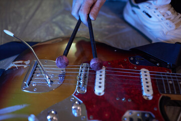Close up shot of male hand holding fiber tip pan sticks tapping electric guitar strings for achieving even rhythmics and harmony during studio recording