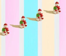 A repetitive wallpaper pattern made of snowmen with a cap and a scarf against the striped pink, peach powder, turquoise and white background. Winter concept. Christmas funny pattern. Minimal concept. 