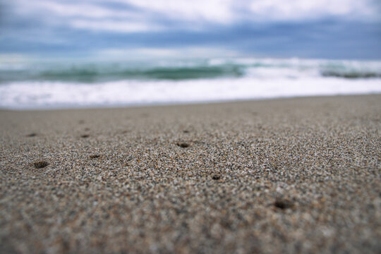 Close up sea sand beach with foam and waves photo. Sand beach surface with selective focus.