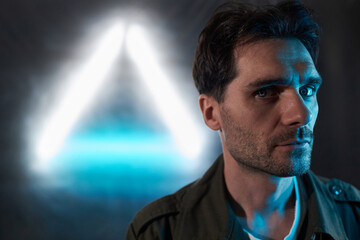 Close up shot of Caucasian brunette male with blue eyes and stubble against fluorescent lamp light looking at camera with face half-turned