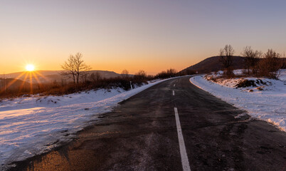 Fototapeta na wymiar Empty asphalt road in rural landscape at sunset. Blue sky above the road. The sun's rays fall on the wet asphalt of the main road. Winter scene.