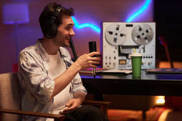 Waist up shot with side view of smiling male podcaster holding professional microphone during interview in studio room