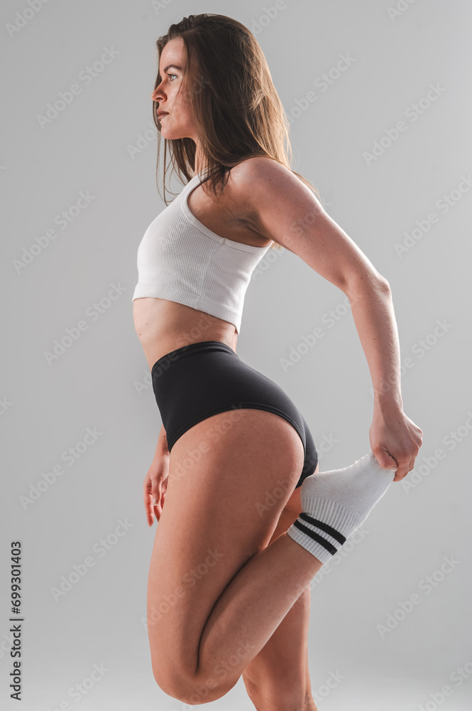 Wall mural Athletic Caucasian woman stretching her quadriceps on a white background. Vertical photo.