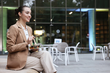 Happy young businesswoman eating lunch on bench outdoors