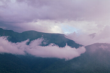Fog and clouds in the mountains against the backdrop of the setting sun, changeable weather in the...