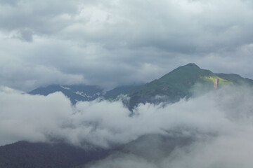 Fog and clouds in the mountains against the backdrop of the setting sun, changeable weather in the...