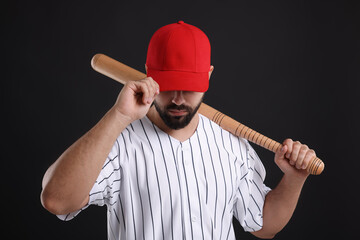 Man in stylish red baseball cap holding bat on black background