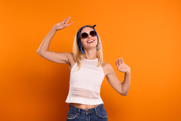 Portrait of smiling hippie woman in sunglasses dancing on orange background