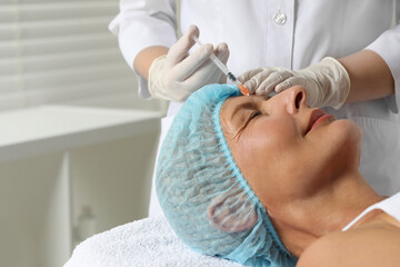 Doctor giving facial injection to senior woman in clinic, closeup. Cosmetic surgery