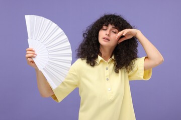 Woman with hand fan suffering from heat on purple background