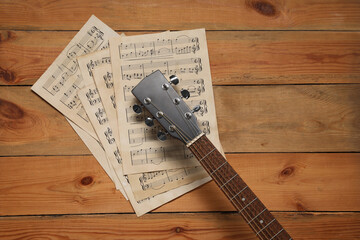 Paper sheets with music notes and acoustic guitar on wooden table, top view