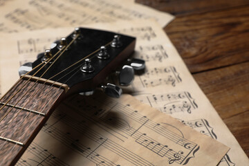 Paper sheets with music notes and guitar neck on wooden table, closeup