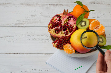 The concept of inspection, analysis, quality control of products, fruits. An assortment of citrus fruits and a hand holding a magnifying glass. Space for copy, horizontal.