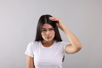 Emotional woman examining her hair and scalp on grey background