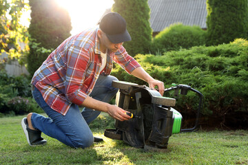 Man with screwdriver fixing lawn mower in garden on sunny day - obrazy, fototapety, plakaty