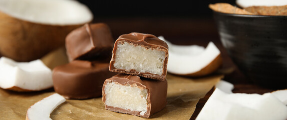 Delicious milk chocolate candy bars with coconut filling on wooden table, closeup. Banner design