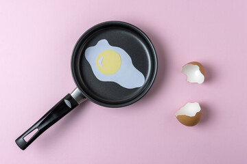 Paper fried egg in small frying pan on pastel pink background. Minimal food concept.