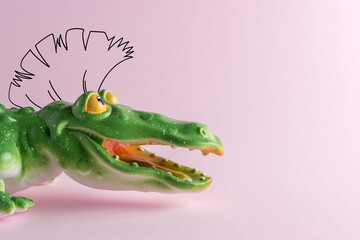 Green crocodile toy with drawing mohawk on pastel pink background. Minimal art concept.