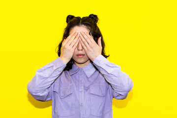 Young latina woman covering her eyes against yellow background