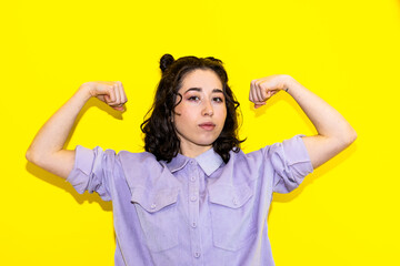 Young Latina woman with raised arms on yellow background. Girl power concept.
