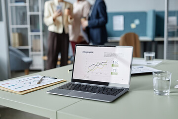 Medium shot with focus on opened laptop displaying business report infographic, water glasses and...