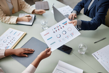 Close up shot of unrecognizable female employee hand passing paper with graphs to coworker during meeting while sitting at office table