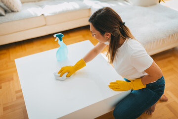 The young woman is cleaning the living room wearing yellow gloves