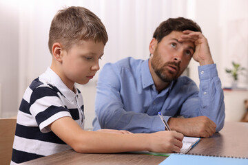 Dyslexia problem. Annoyed father helping son with homework at table indoors, selective focus