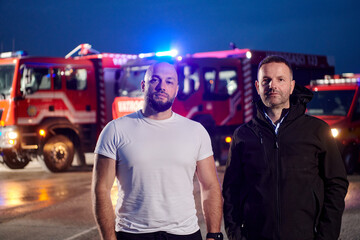 Group of firefighters, dressed in civilian clothing, stand in front of fire trucks during the...