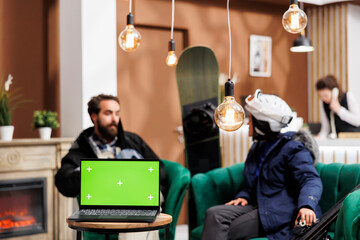 Couple in winter clothing in lounge area sitting behind laptop displaying blank copyspace template....