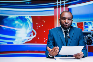 News reporter delivering breaking news on media segment in newsroom, reading important headlines of the day on international tv program. Man journalist presenting daily events live. - obrazy, fototapety, plakaty