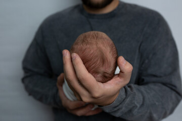 Father holding head of her newborn baby in hands. Loving father hand holding cute sleeping newborn baby child. Beautiful conceptual image of parenthood