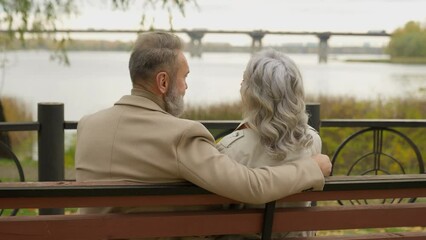 Rear back view happy senior couple family sit on bench love retirement mature woman man enjoy romantic date in city park middle aged Caucasian male and female grandparents talk relax together outdoors