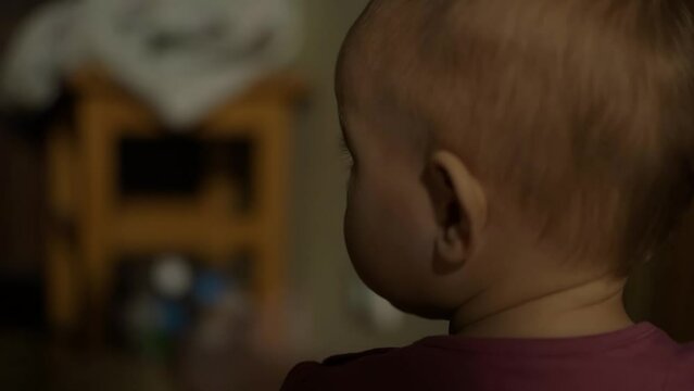 a small fair haired child with long eyelashes sits with his back to the camera and slowly and hesitantly begins to crawl into the open arms of his mother.