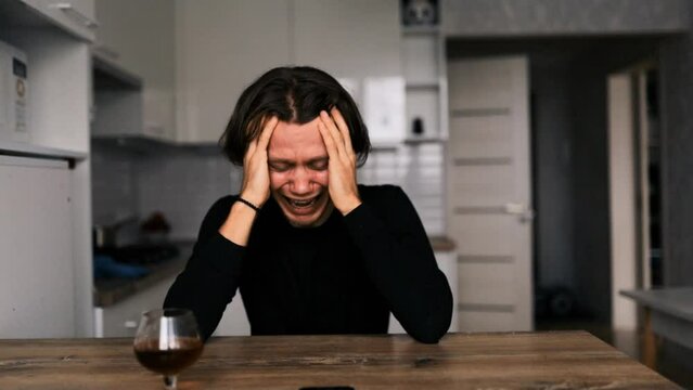 hysterical man crying at home at table with alcohol, mental illness concept.